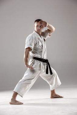 A man in a karate uniform with a black belt is standing on one leg.