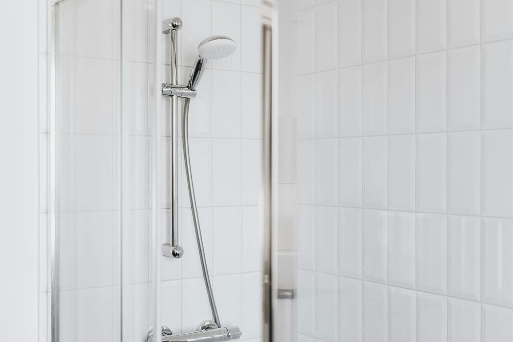 Shower with white tile walls and a silver shower head and controls.
