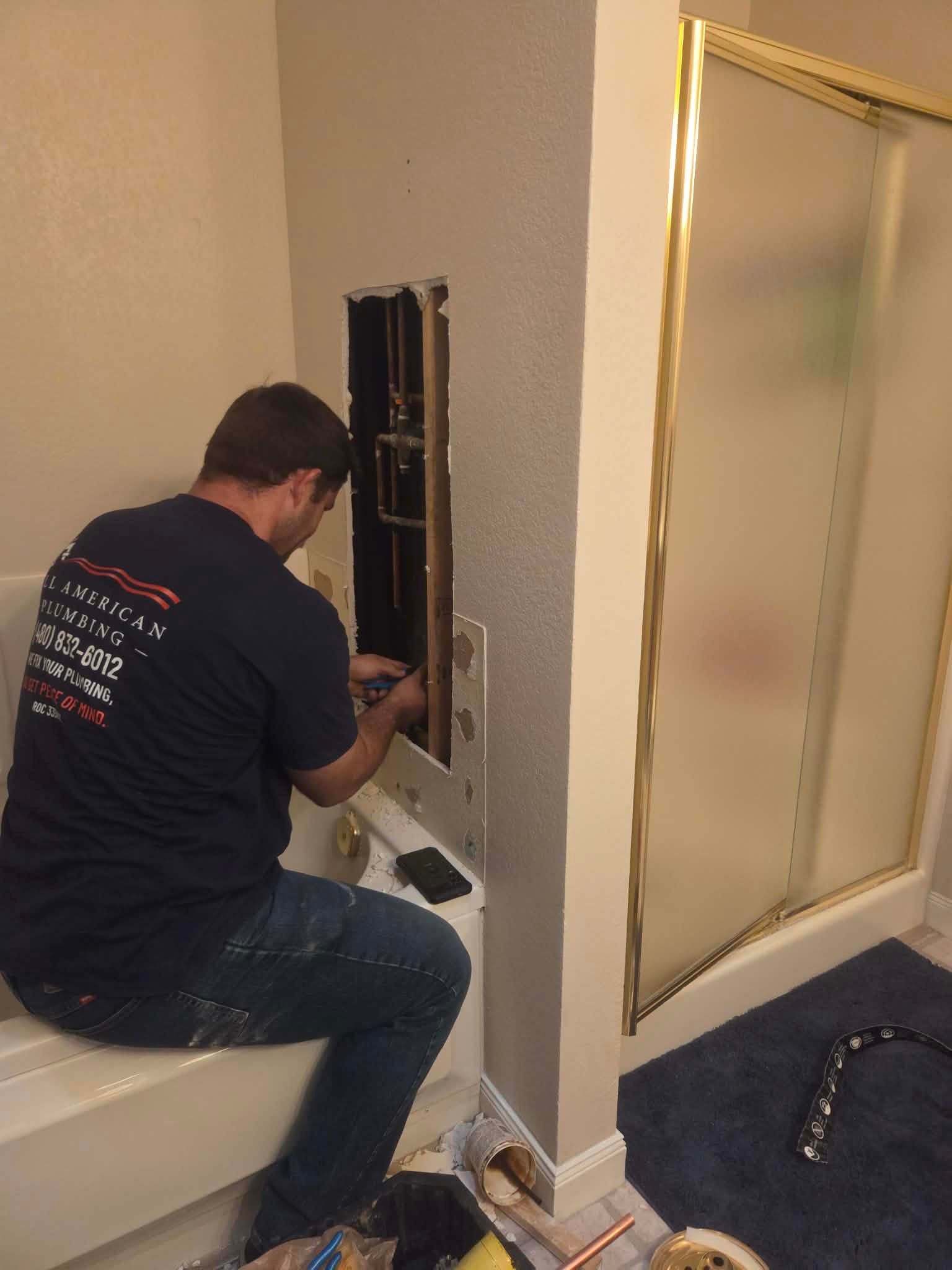 Worker installing wiring in a wall, kneeling beside an open electrical box in a hallway.