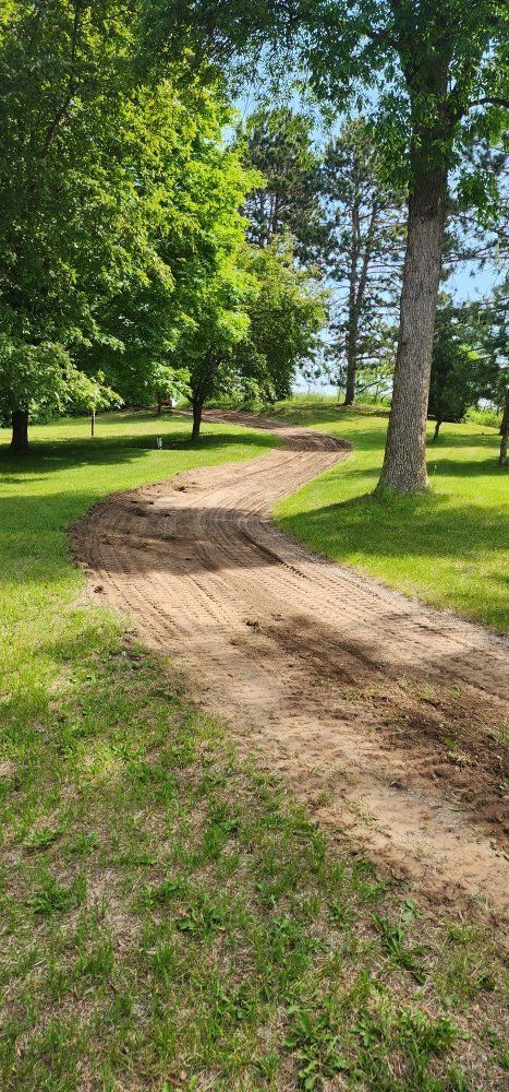 Dirt path winds through a grassy park, trees in background, sunny day.
