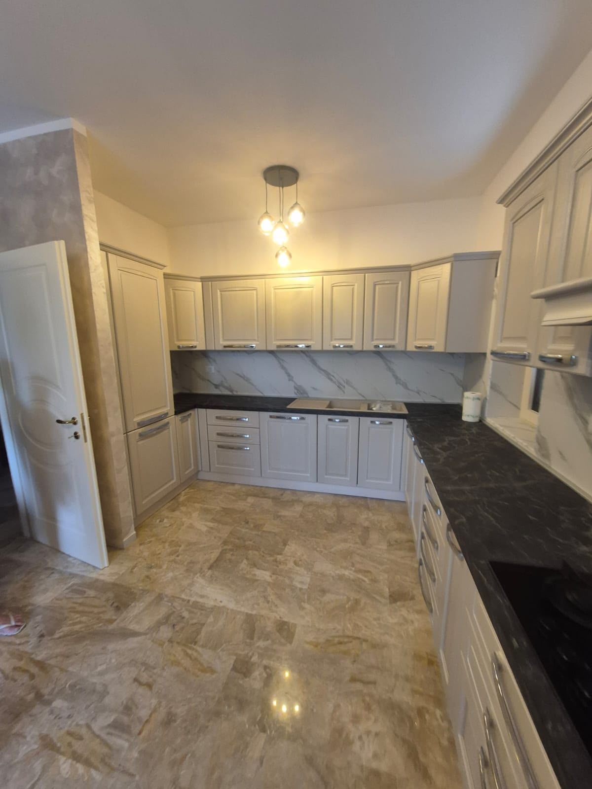 Cucina moderna vuota con mobili bianchi, ripiani neri e pavimento in piastrelle beige.