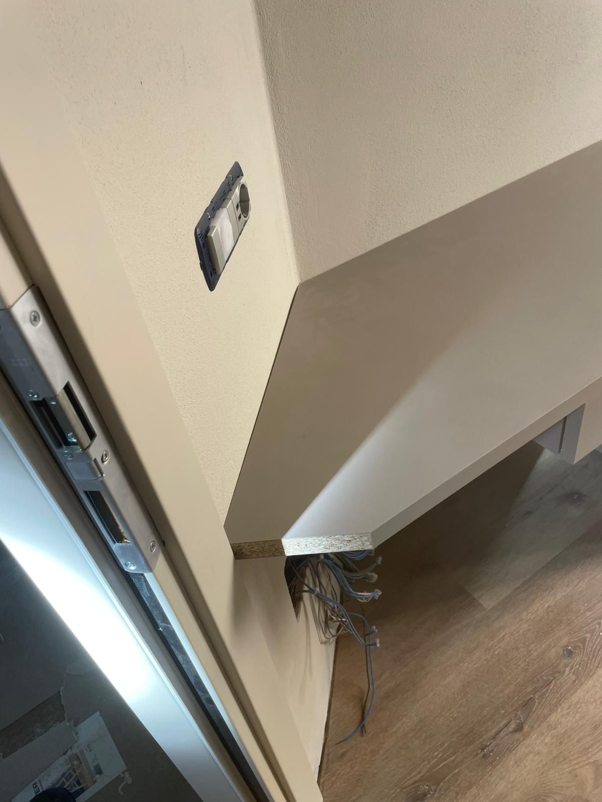 Angolo del corridoio con un bordo del muro danneggiato e fili scoperti vicino al pavimento.
