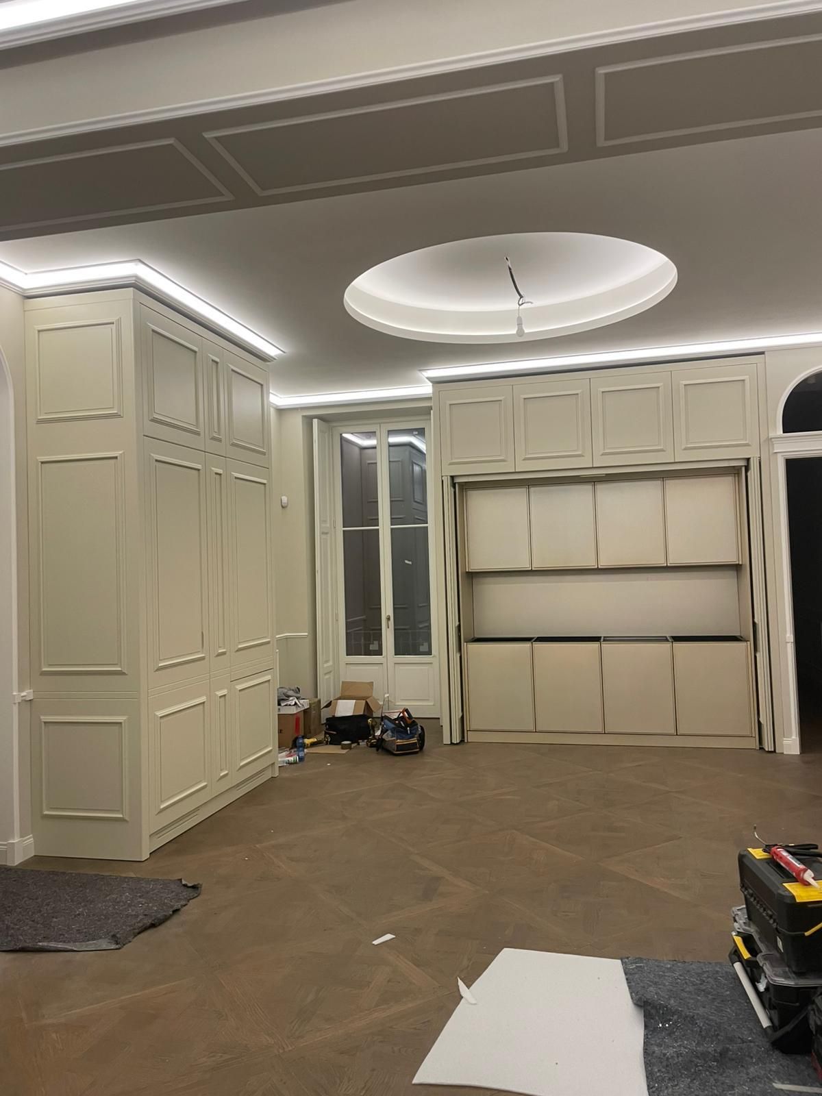 Stanza vuota con armadi a muro beige, faretti a incasso sul soffitto e moquette marrone; attrezzi e materiali sul pavimento.