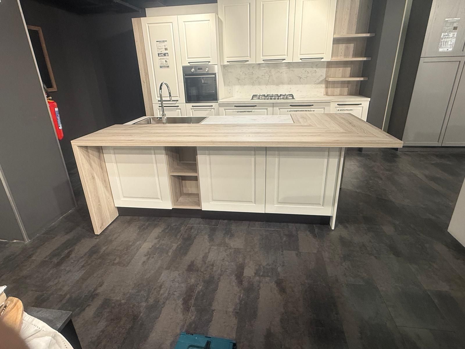 Cucina moderna con grande isola, mobili bianchi e pavimento in legno scuro.