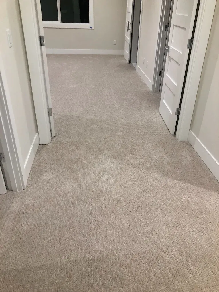 Hallway with beige carpet, white doors and trim, a window at the end.