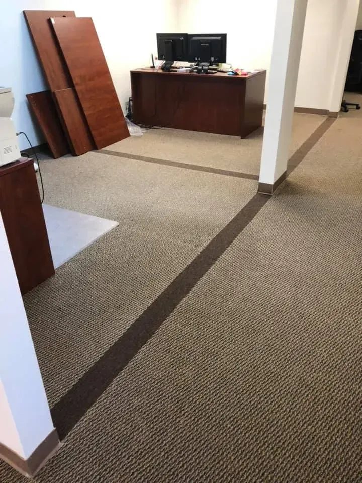 Office interior with carpet and brown trim. Dark wooden desk and disassembled furniture visible.