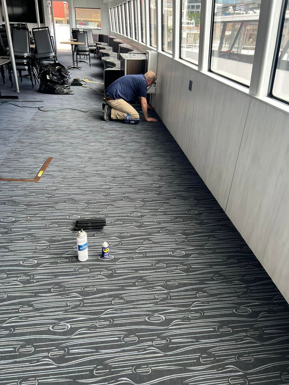 Carpet repair technician , kneeling near a wall and a window, performing a carpet repair
