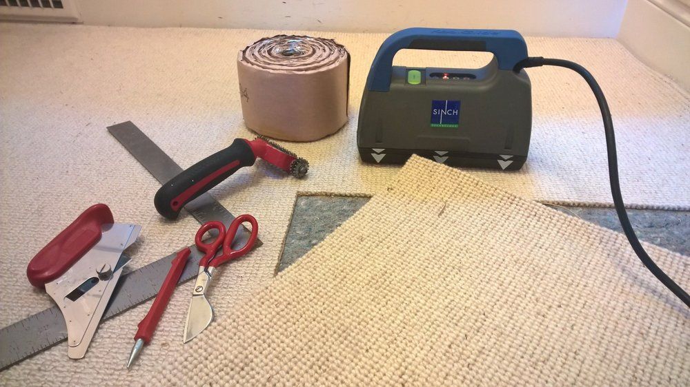 Carpet installation tools and materials: seam roller, knife, scissors, and carpet, in a room.