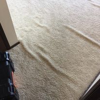 Beige carpet with a visible ripple. Corner of a dark wooden door frame on the left.
