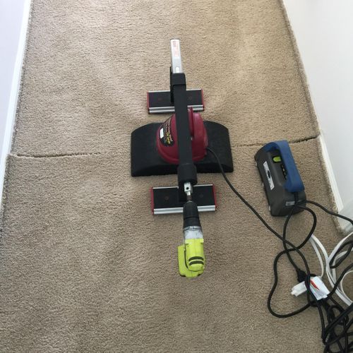 Carpet cleaning tool with a drill attached, on beige carpet near a power outlet.