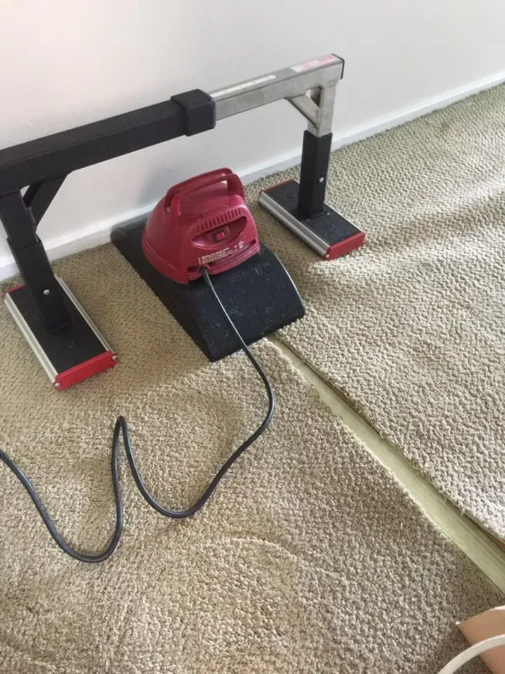 Carpet stretching tool set next to a white wall. The tool includes a red iron, black bars, and silver bars.