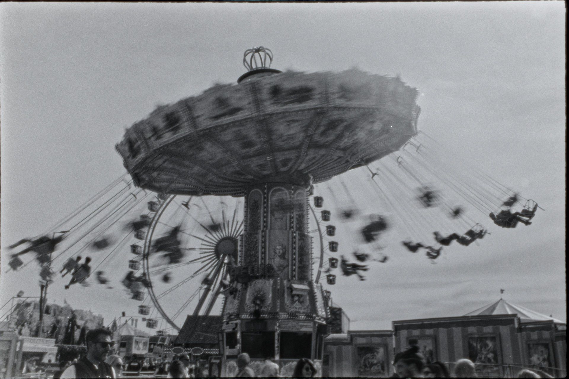 A black and white photo of people riding a carousel at an amusement park.