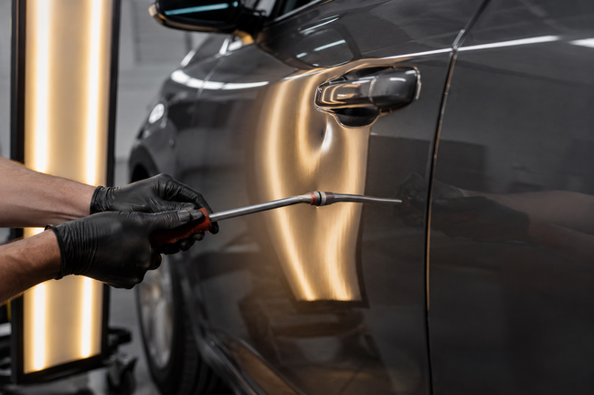Gloved hand polishing a dark car door with a detailing tool, reflecting light in a garage