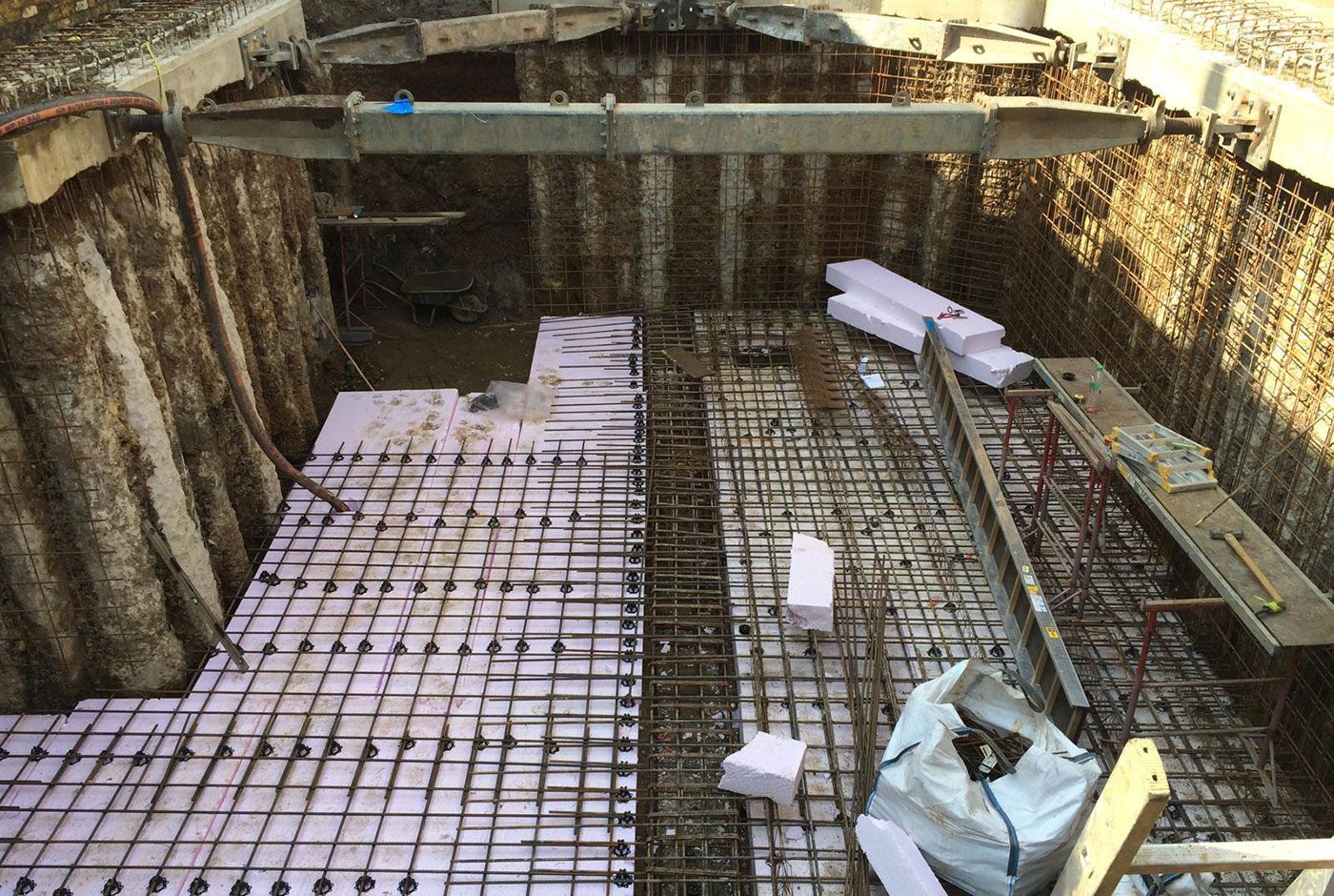 External construction site with a deep excavated pit, rebar grid, and wooden formwork walls.