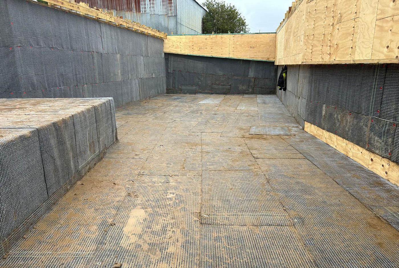 Empty construction area with dark retaining walls and wood panel sections..