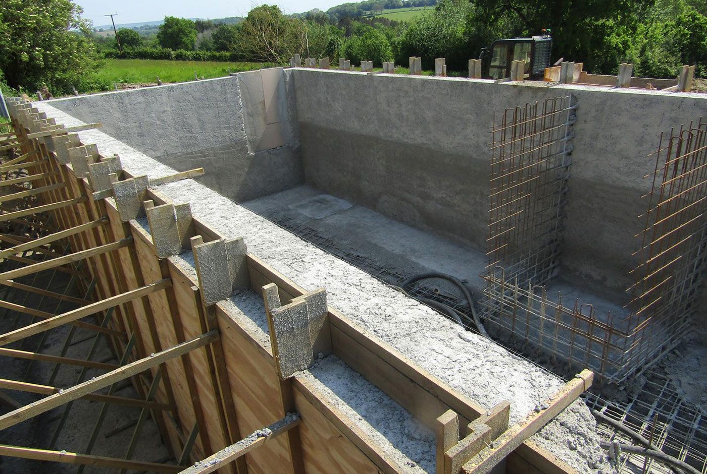 Outdoor concrete rectangular pool under construction with wooden formwork in a countryside location.