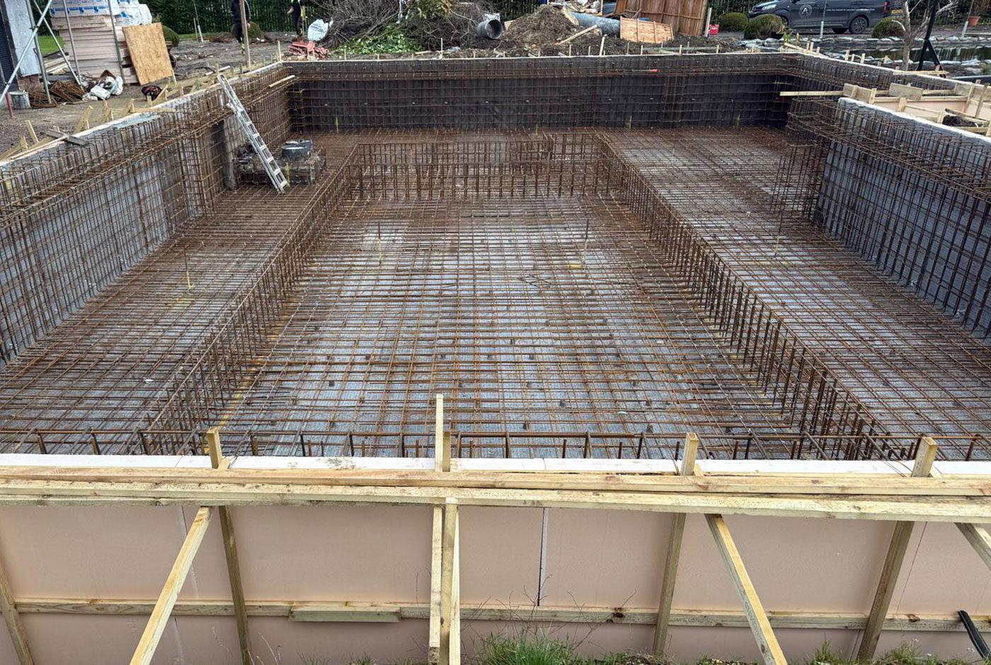 Large rectangular foundation structure with steel rebar grid and wooden formwork, viewed from above.