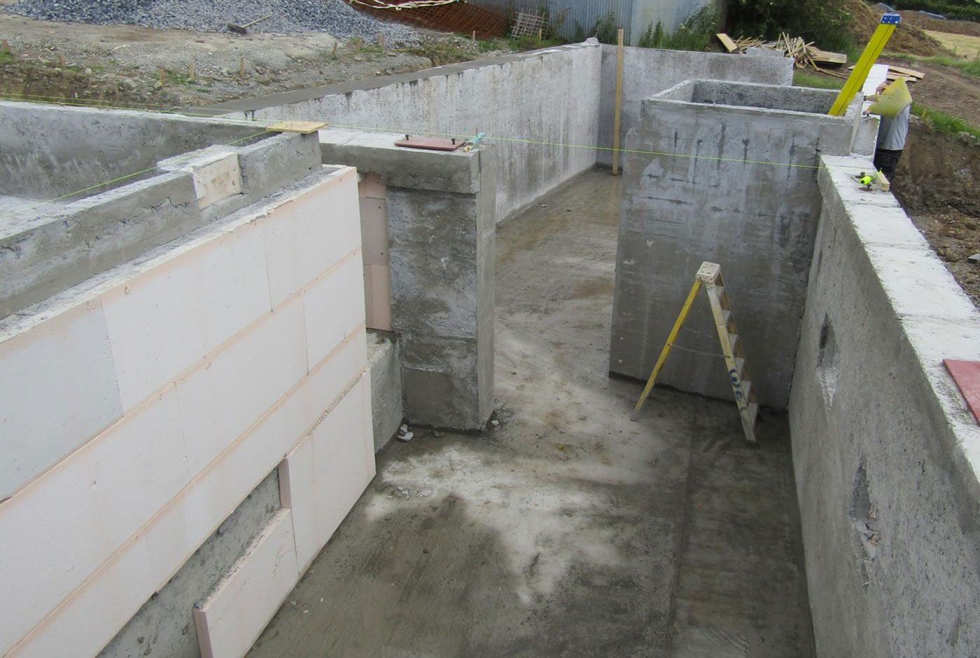 Partially built concrete basement or foundation with walls, floor, step ladder and leveling lines.