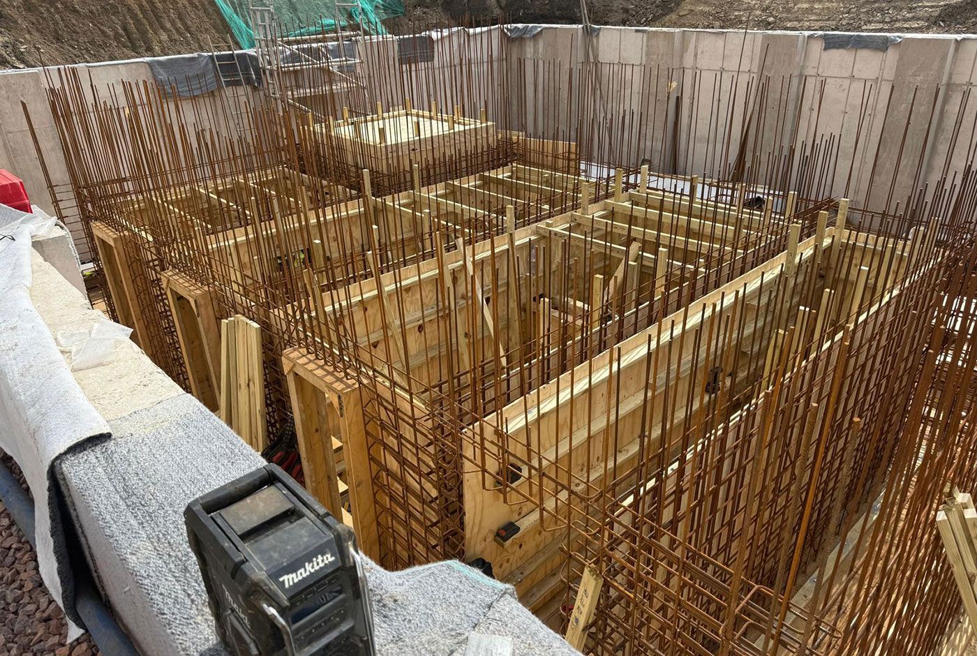 Rebar foundation layout with wooden forms and concrete walls at a construction site.