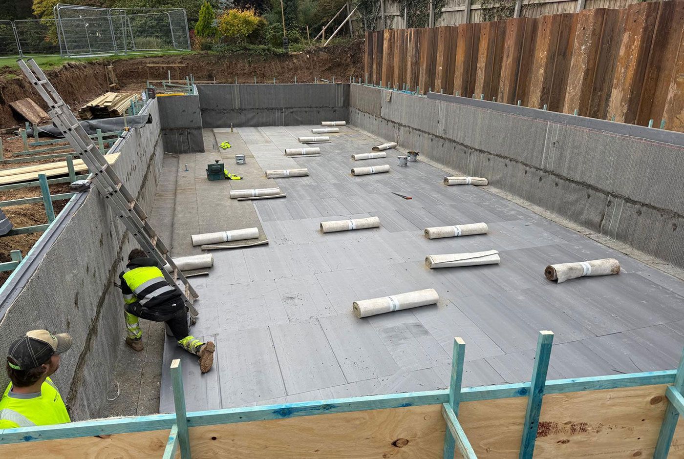 Construction workers in a foundation structure being built, with rolls of material positioned over the base. 