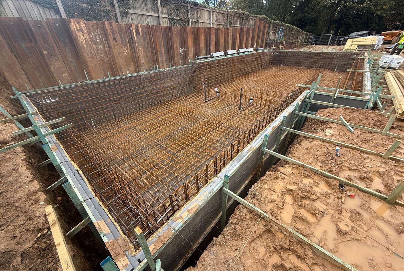 Construction excavation site with rebar mesh, timber framework, and muddy soil around a deep pit