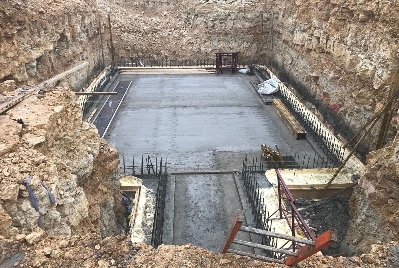 Concrete foundation slab with rebar within an excavation pit surrounded by rough rock walls.