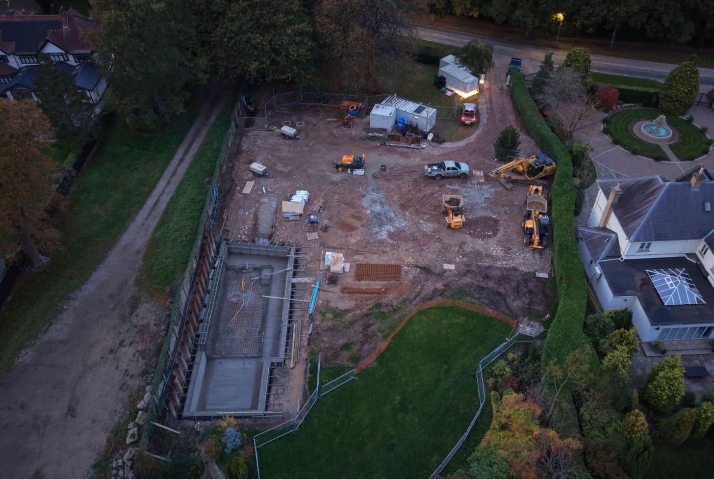 Aerial view of a muddy construction site in poor light with a foundation structure in progress, machinery, and a house.