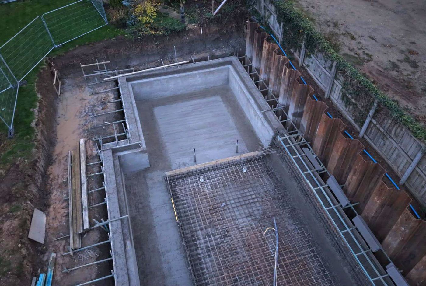 Overhead view of an excavation site with a rectangular concrete foundation under construction and retaining walls.