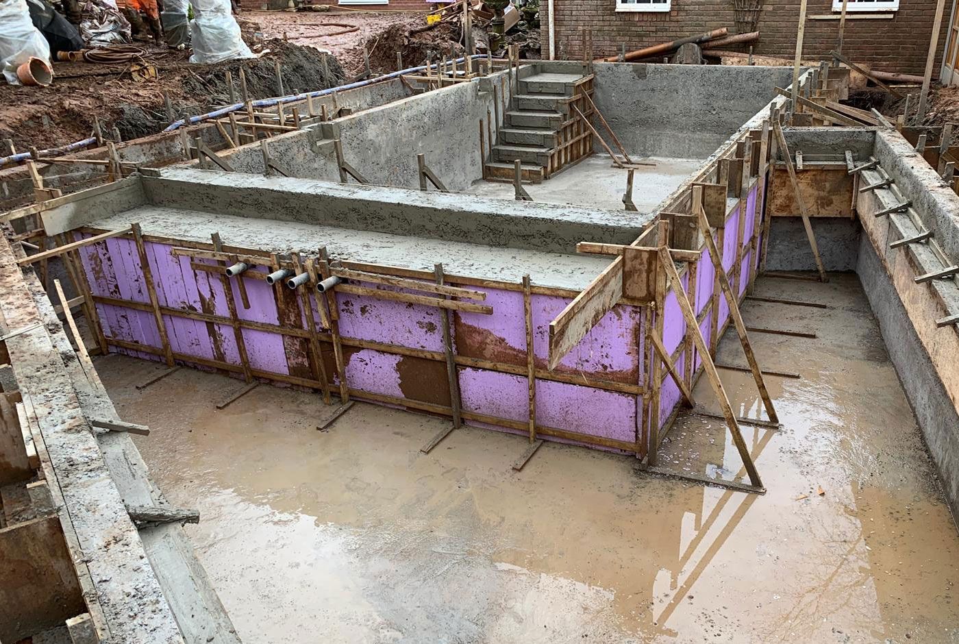Concrete swimming pool shell under construction next to a house, with purple coloured exterior.