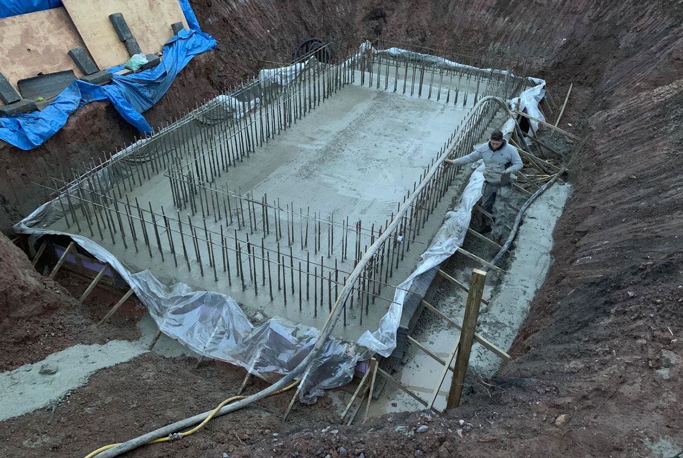 Concrete foundation slab with rebar pins in an excavated construction site with sloping walls, a worker dressed in grey.
