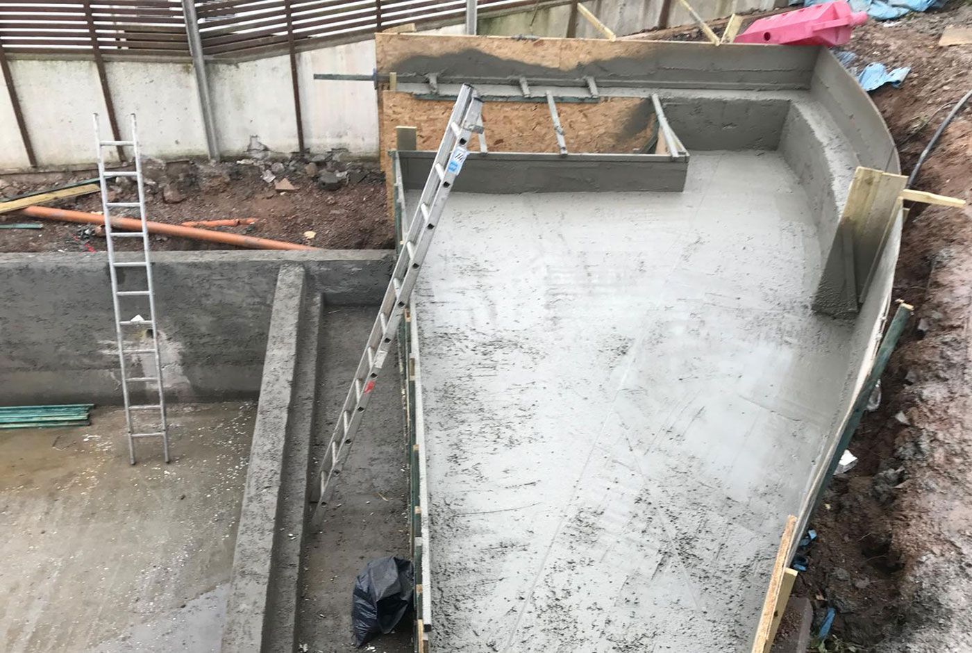 Overhead view of a concrete foundation structure with several levels, retaining walls and two metal ladders.