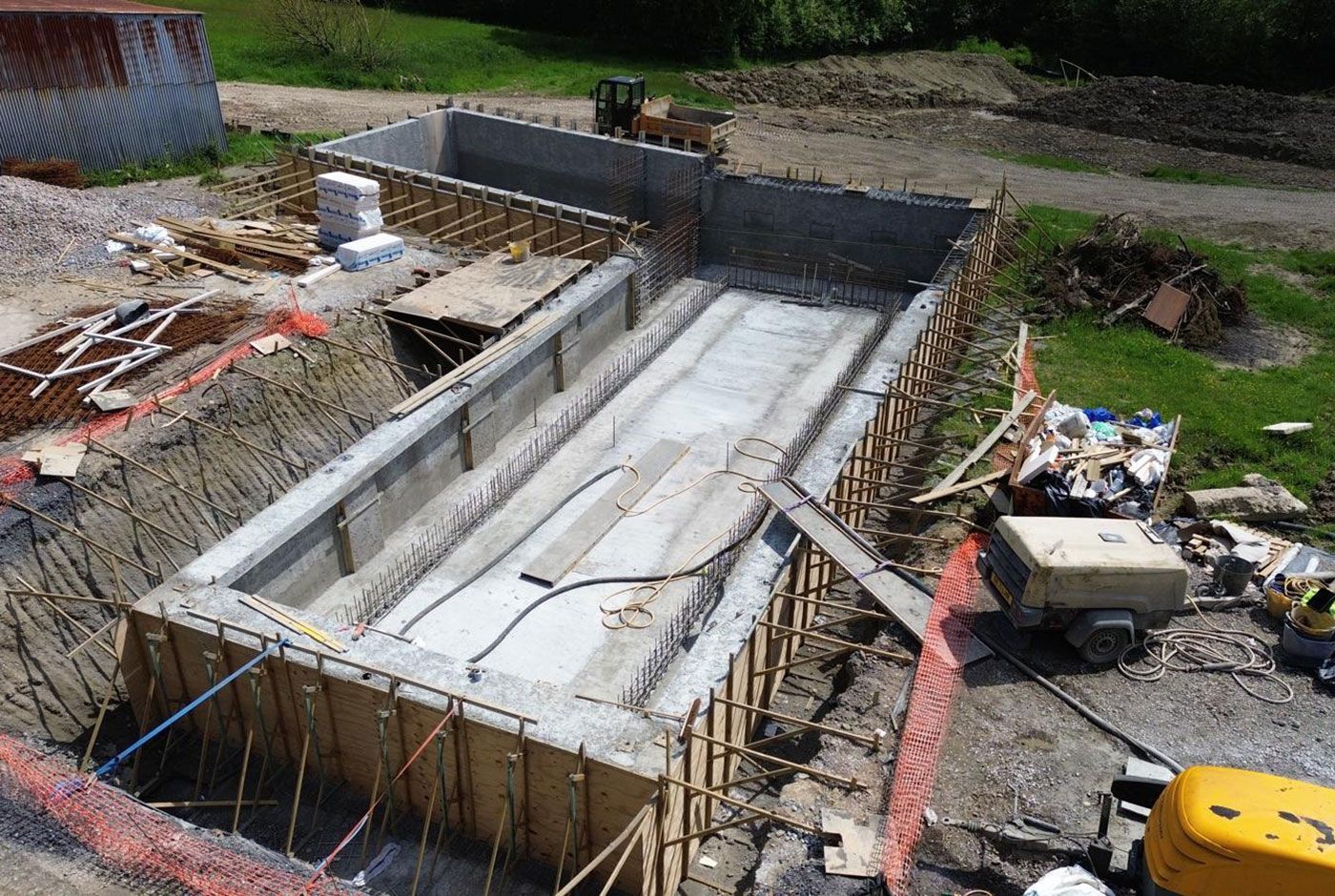 Construction site with a concrete foundation structure and rebar walls being built, surrounded by building materials.
