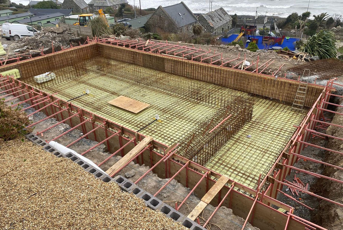 Large rectangular excavation site at a coastal location, with a rebar foundation under construction.