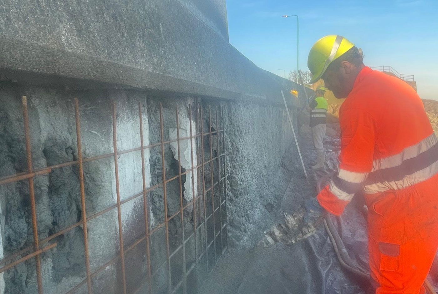 Worker in orange hi-viz spraying concrete onto a damaged concrete wall and rebar.