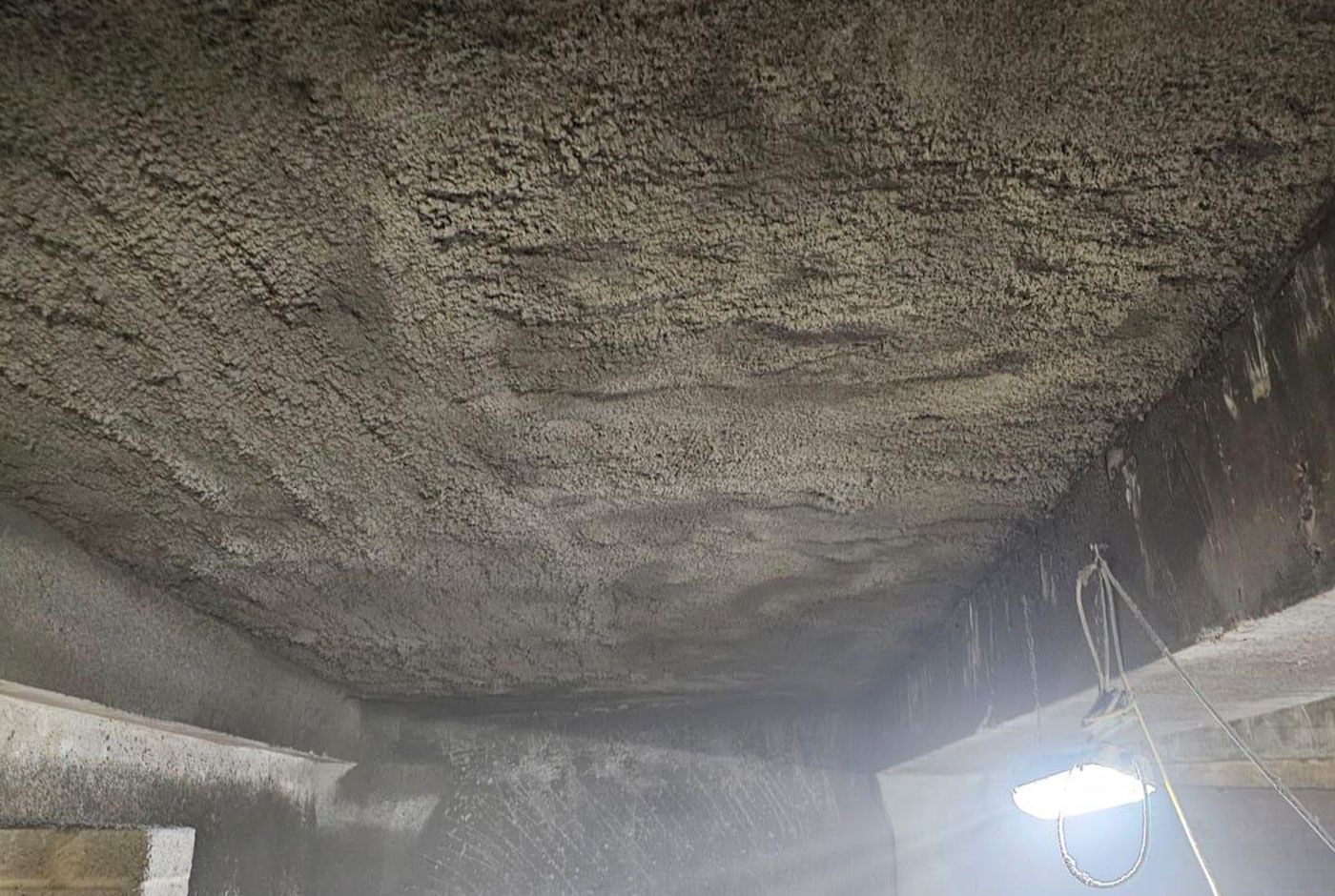 Rough concrete ceiling with a hanging light  in a dim interior space.