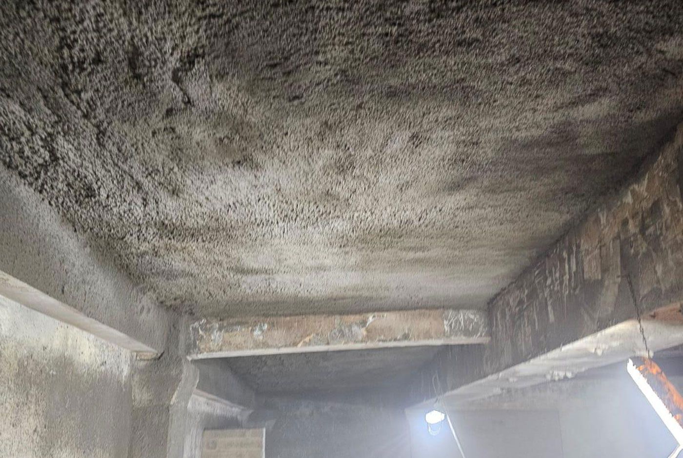 A rough concrete ceiling with exposed beams in an enclosed concrete space, lit with bright lights.