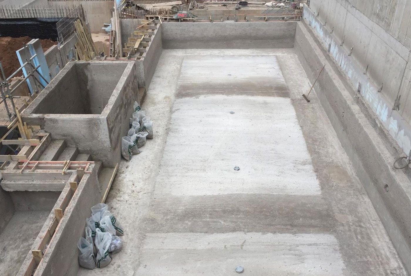 Construction site of a deck-level concrete pool shell, with lots of construction materials visible.