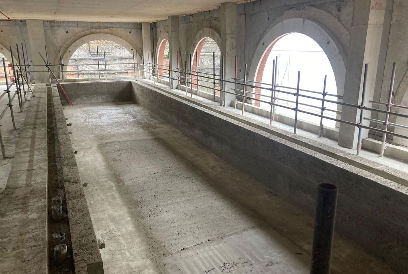 Long indoor swimming pool shell built in a period property with large arched windows.