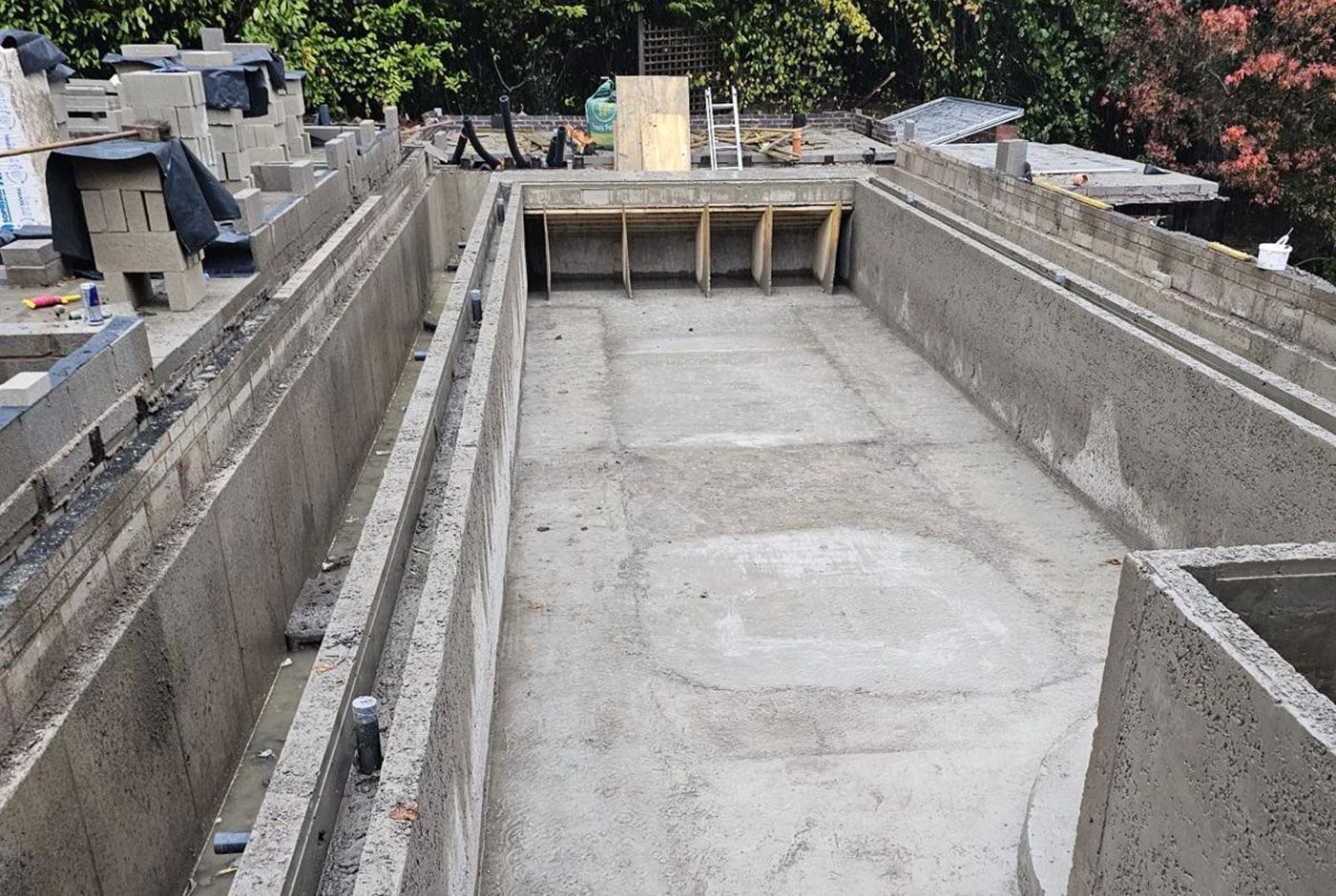 Concrete foundation excavation with retaining walls and wooden formwork at a construction site.