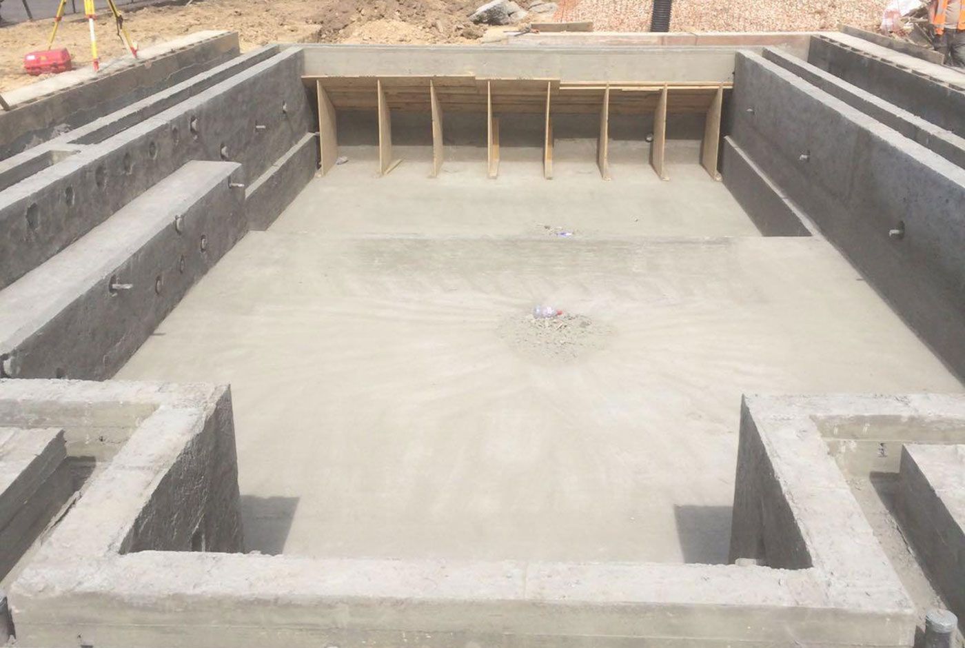 Concrete shell of a deck-level swimming pool under construction with grey walls and unfinished floor.