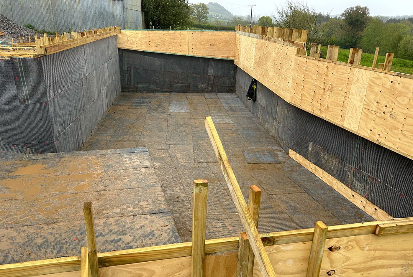 Construction site for a deep foundation pit with wooden braces and black retaining walls.