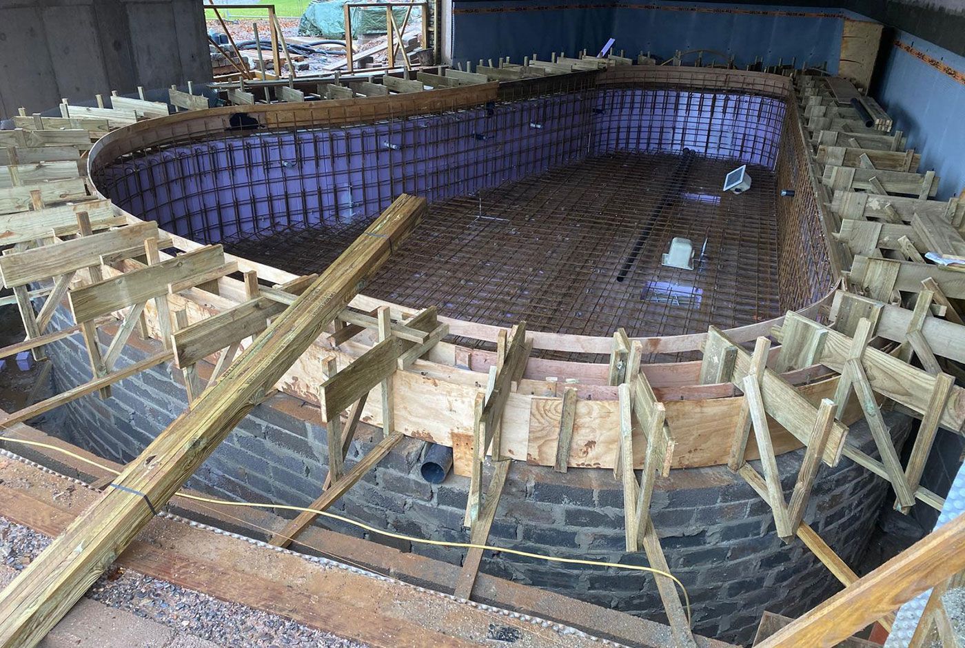 Under-construction circular pool with metal grid on the walls and base, wooden framework, brick surround.