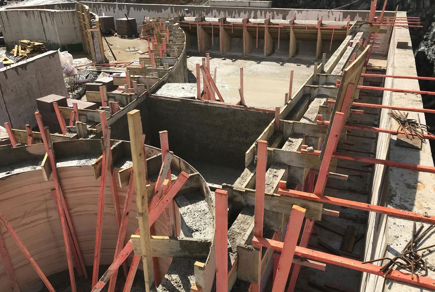 Outdoor pool under construction site with red support braces and wooden formwork creating intricate shapes.