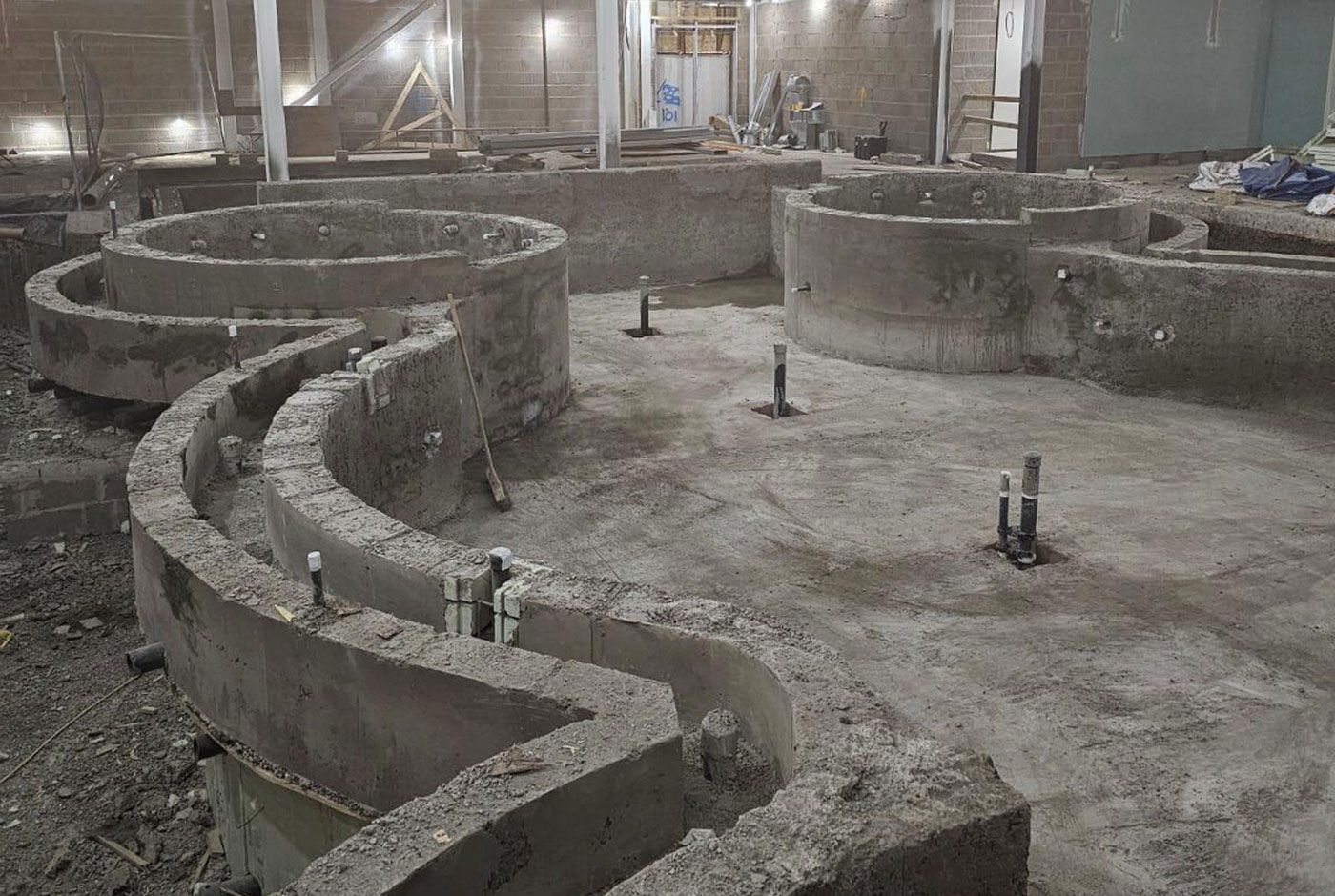 Overhead view of curved concrete foundation walls of an indoor pool in an unfinished construction site.