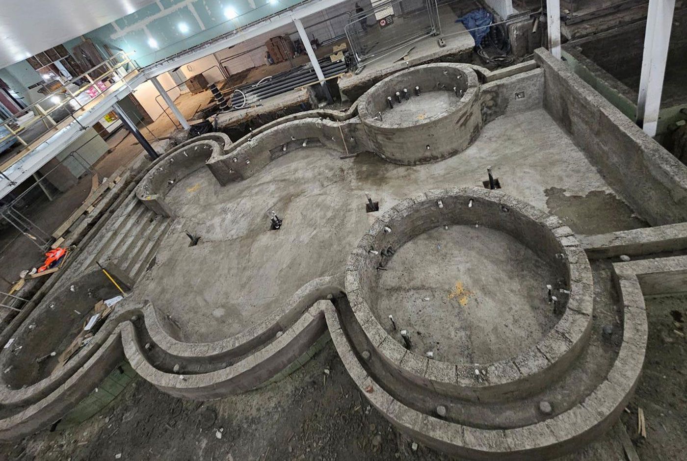 Overhead view of an Indoor pool construction site with large circular forms at a sports complex.