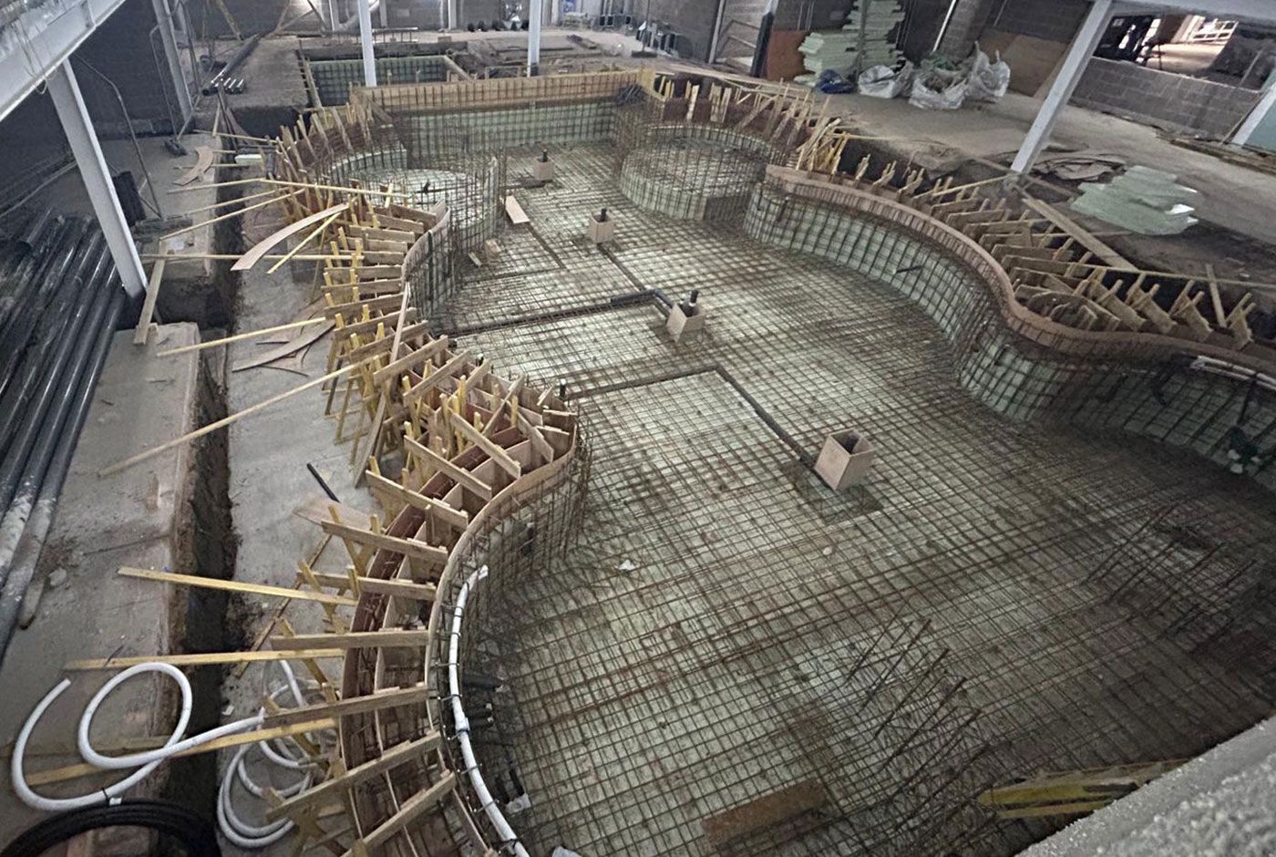 Overhead view of an indoor curved concrete pool foundation under construction with rebar and wooden formwork