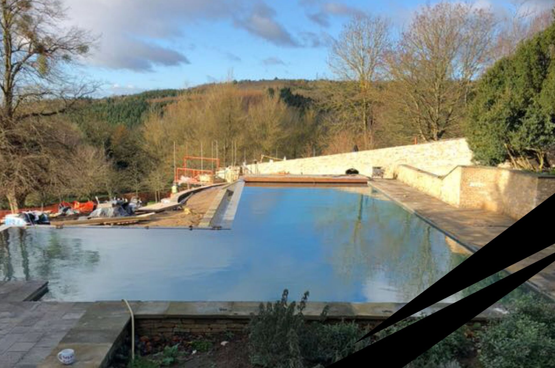 An outdoor infinity swimming pool under construction, with blue water, concrete walls, natural landscape in the background.