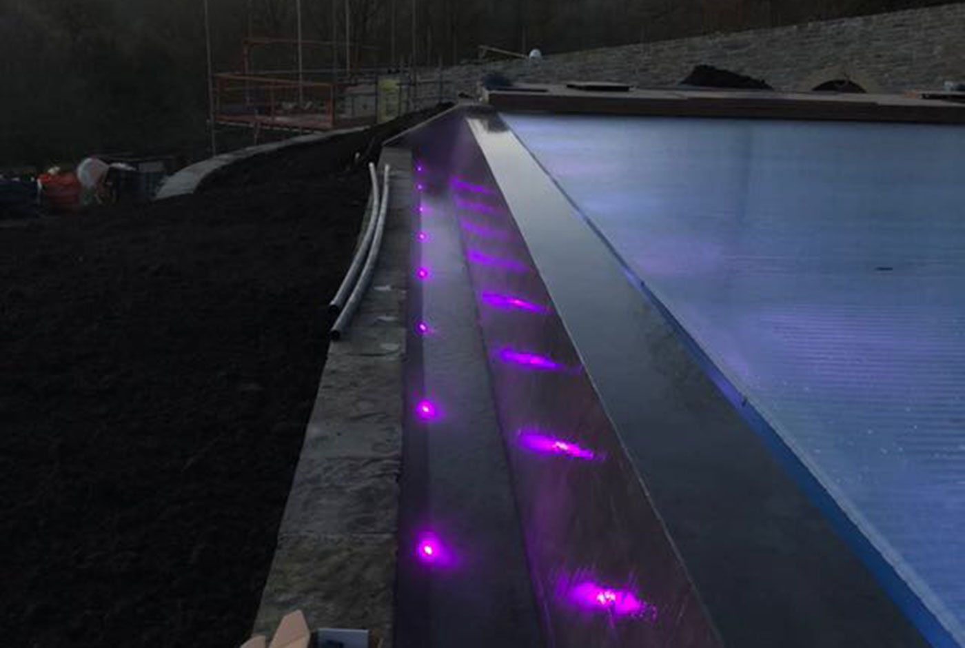 Purple lighting along the edge of an infinity pool at night.