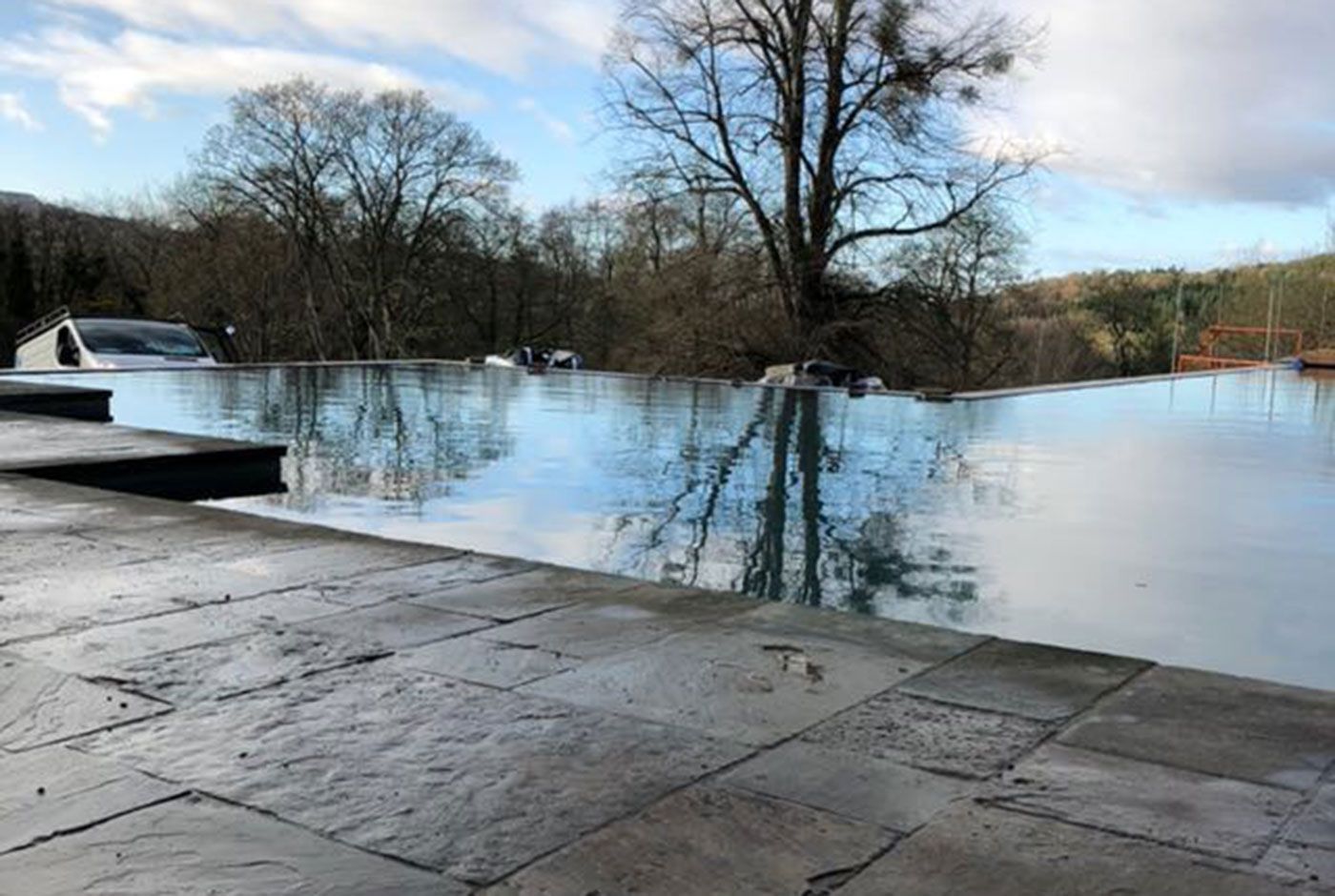 An infinity pool with trees reflected in calm water under a blue sky