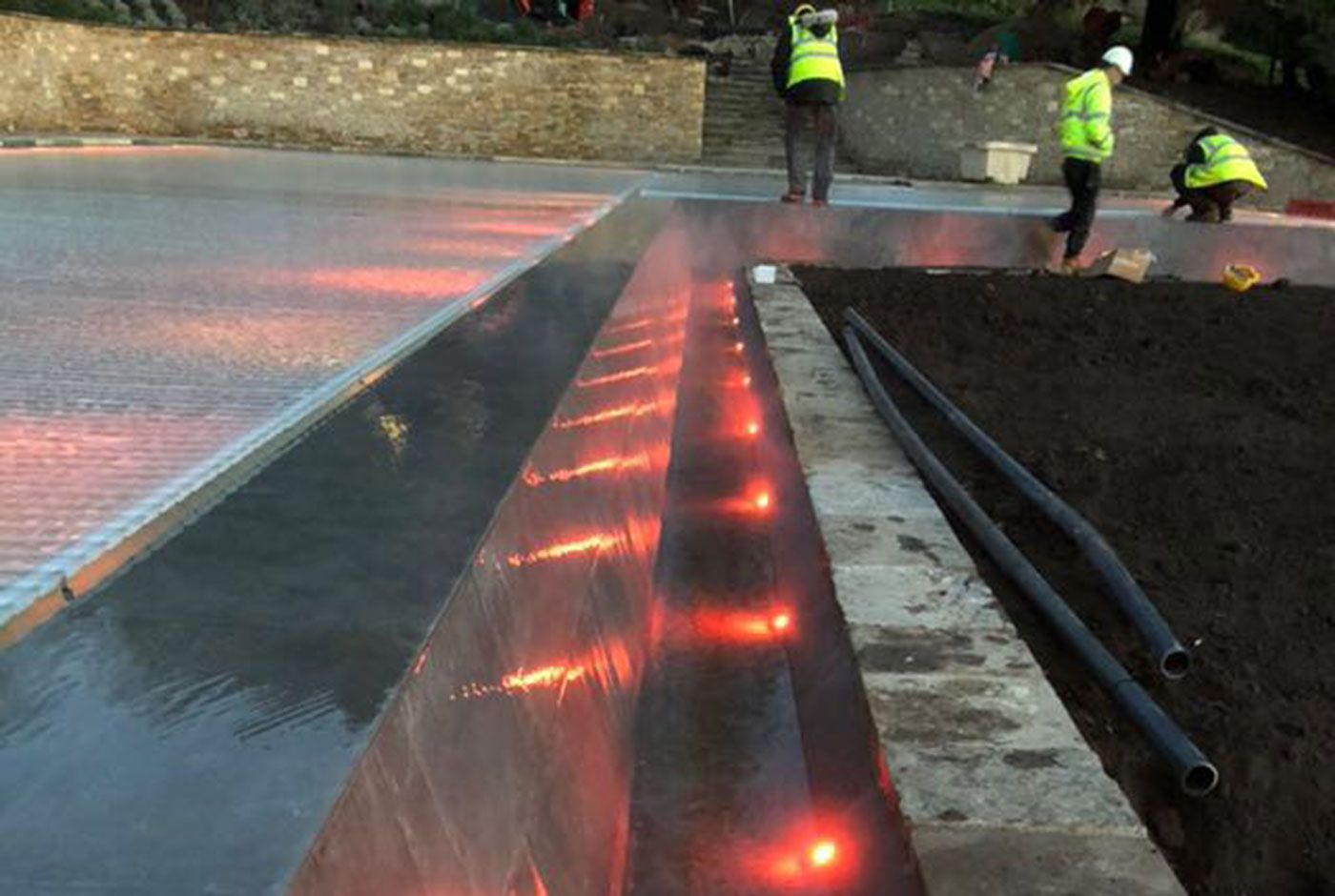 Red lighting along the edge of an infinity pool at night, with three construction workers completing their job.